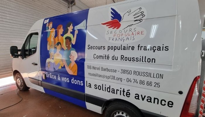 Côté gauche d’un camion floqué aux couleurs du Secours Populaire, avec une illustration colorée symbolisant l’entraide et le bénévolat.