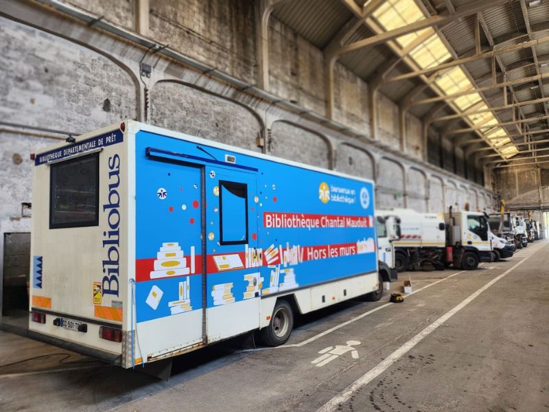 Flanc droit du bibliobus floqué à Grenoble, visuel illustré de livres sur fond bleu, ton joyeux et moderne.
