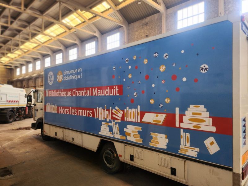 Bibliobus floqué côté gauche, avec visuel coloré et graphique, livres empilés et livre ouvert.